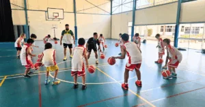 Children participating in a Little Boomers basketball session with their coach on the court