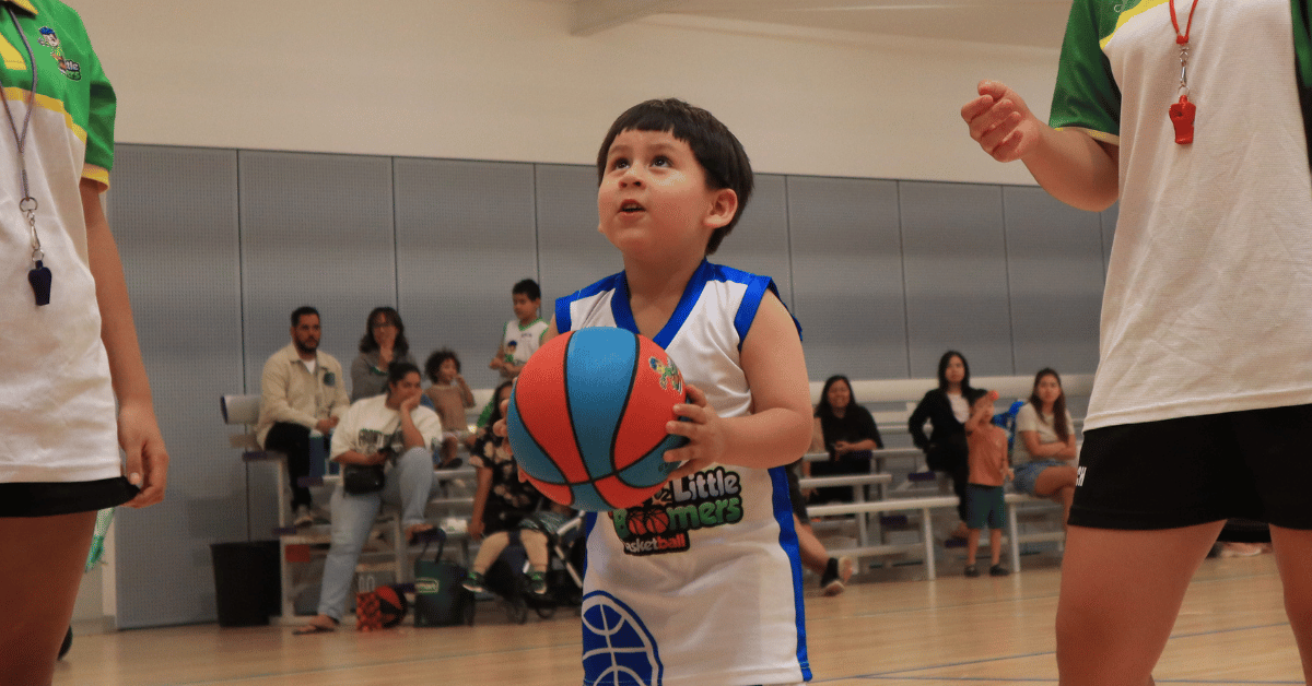 Child preparing to shoot a basketball during a Little Boomers Basketball class inside an indoor court.