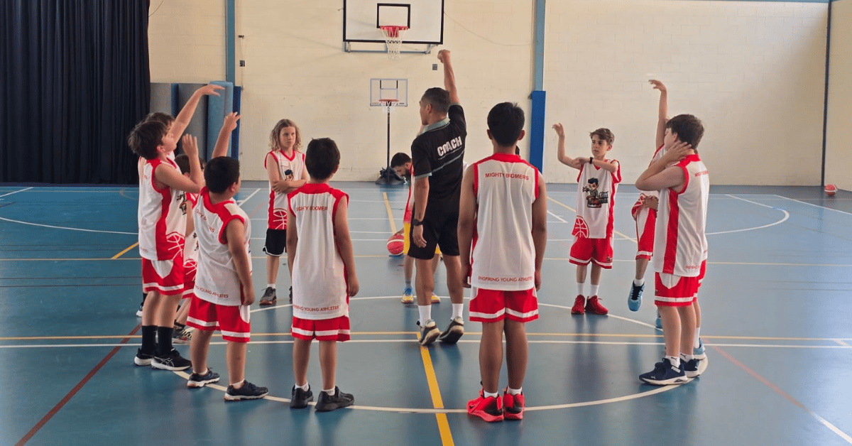 Children participating in a Little Boomers basketball session with their coach on the court