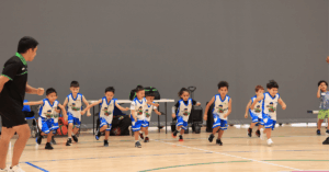 Children participating in a Little Boomers Basketball training session, running across the court during a fun basketball drill.