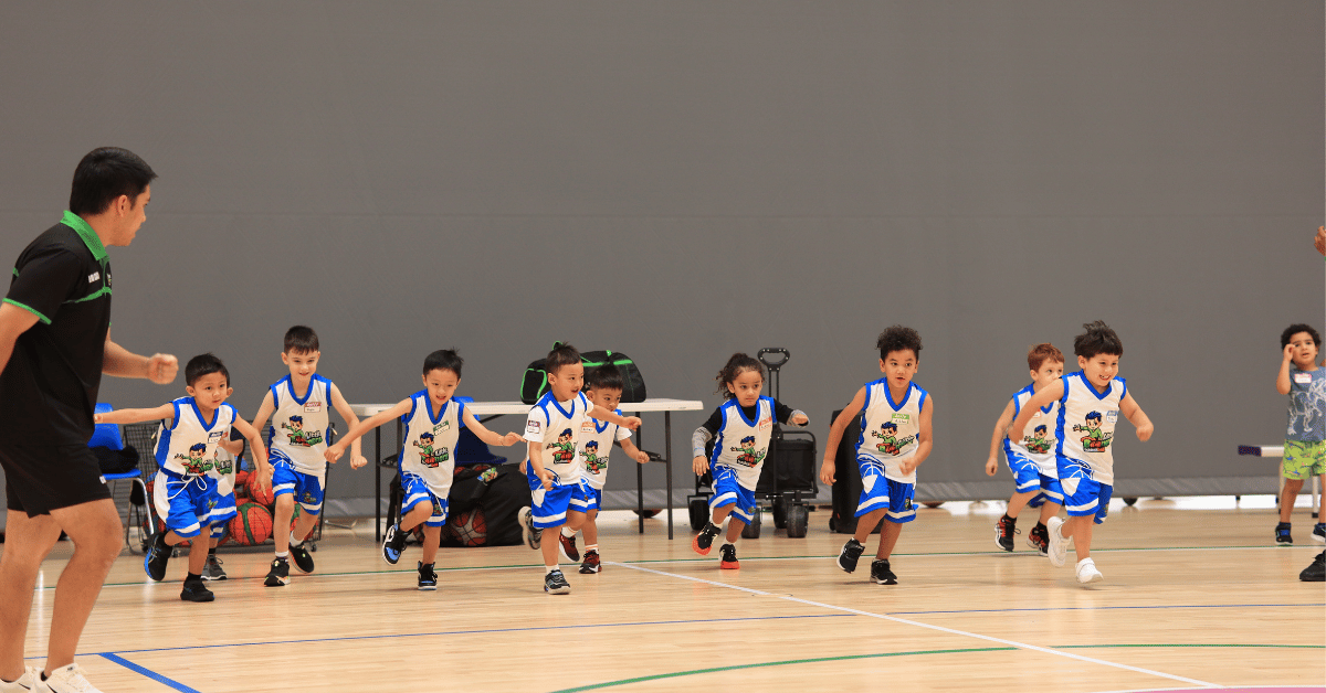 Children participating in a Little Boomers Basketball training session, running across the court during a fun basketball drill.